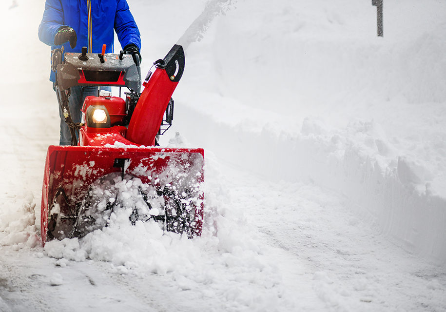 Man clearing or removing snow with a snowblower on a snowy road detail.